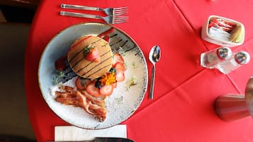 Un plato de desayuno con tortitas, fresas y tocino sobre un mantel rojo.