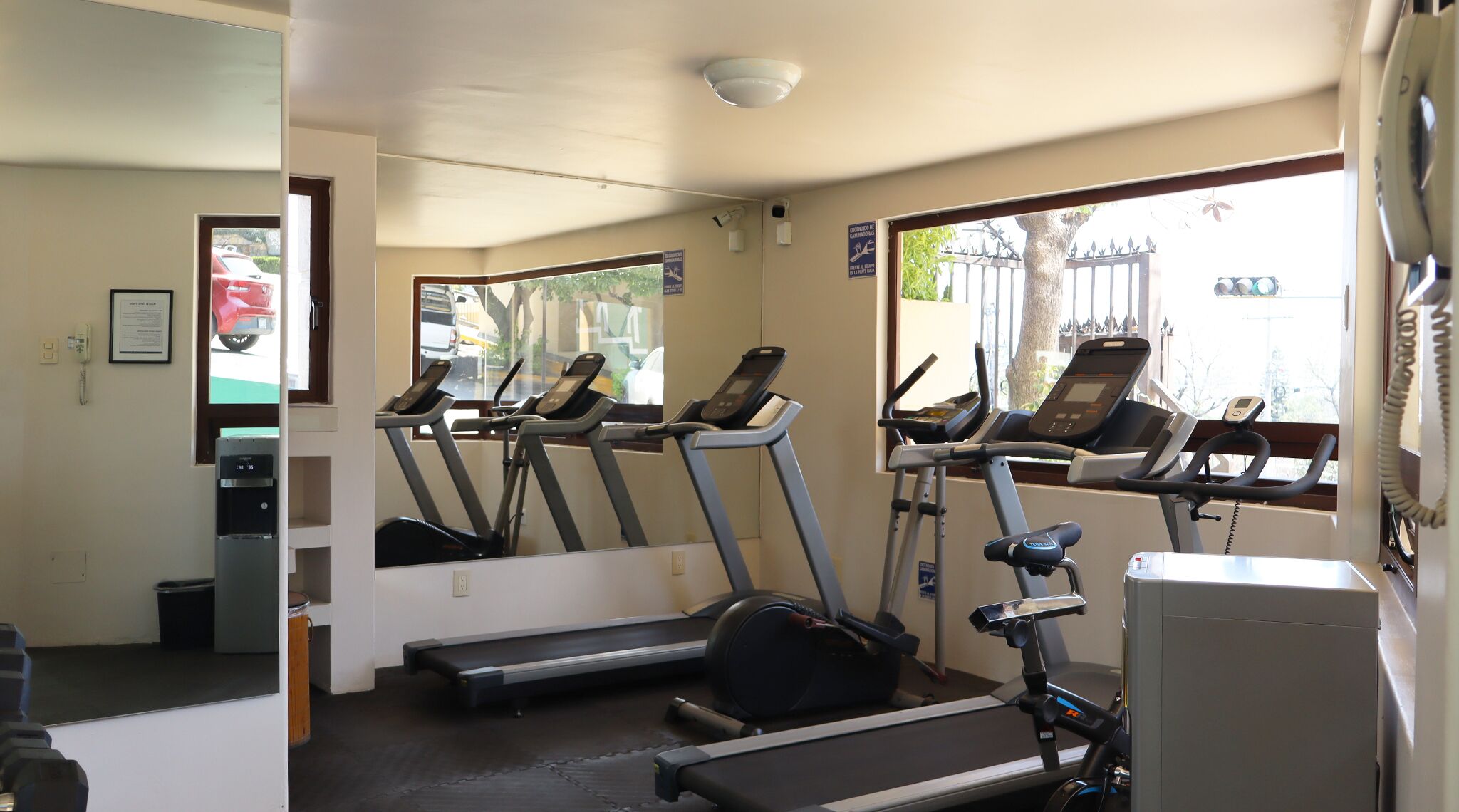 A gym with treadmills, a water dispenser, and a mirror reflecting the outside view.