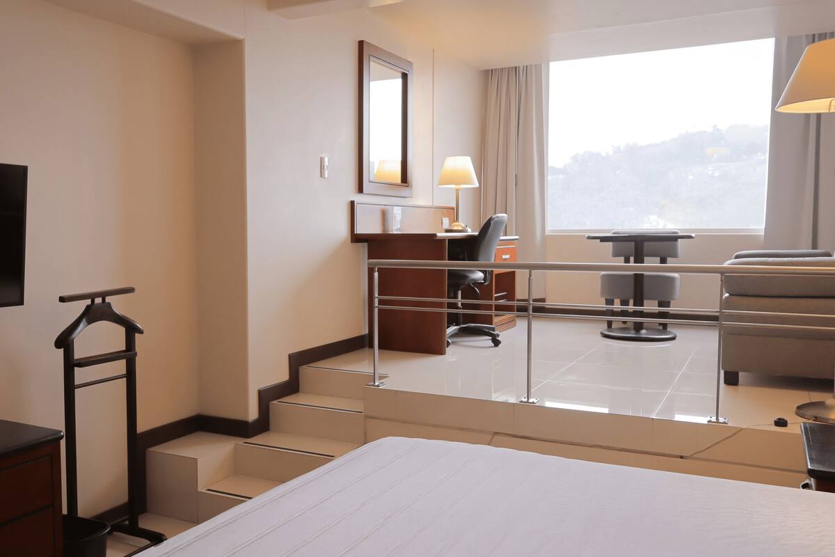 Une chambre d’hôtel comprenant un lit, une télévision, un bureau avec une chaise, une fenêtre donnant sur un paysage agréable et un escalier.