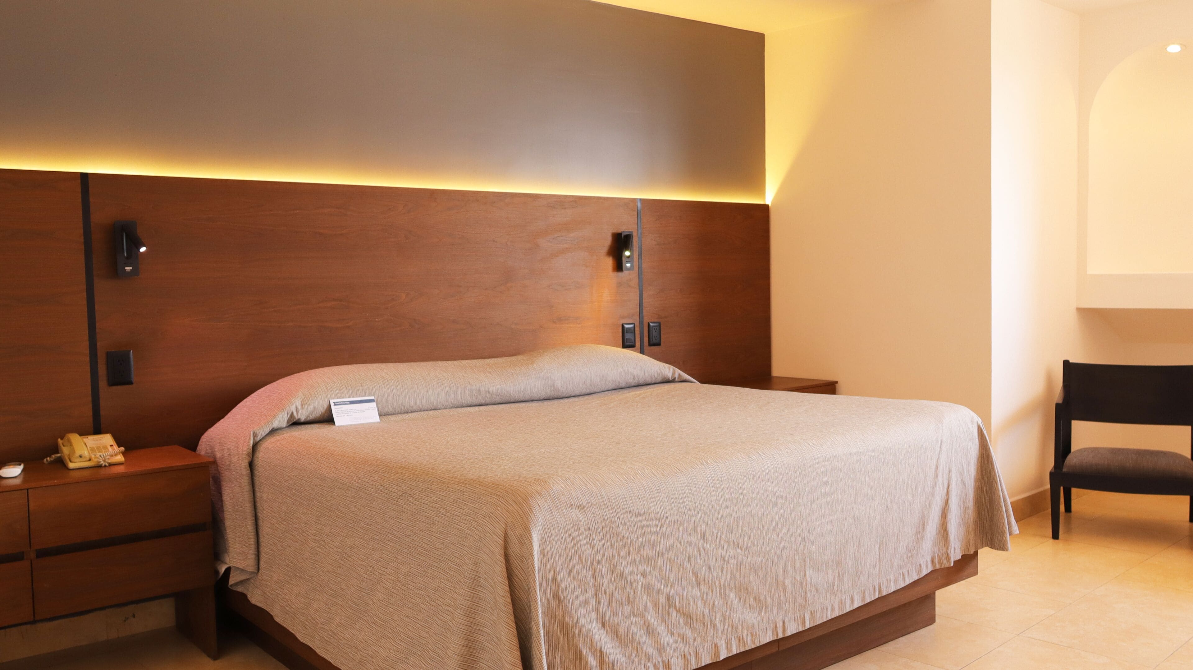 A neatly made bed with a wooden headboard, bedside tables with lamps, and a chair.
