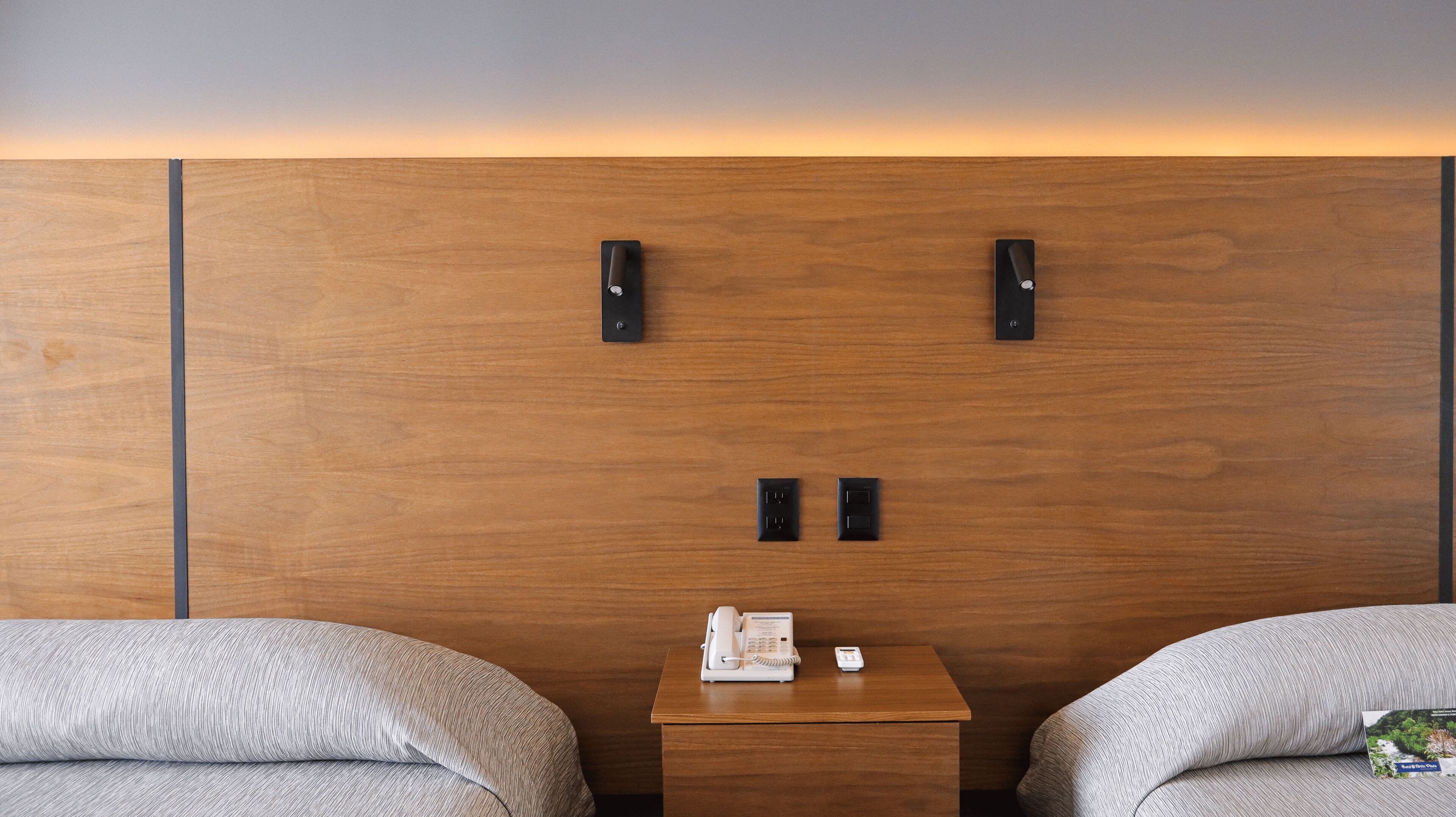 Een hotelkamer met een houten hoofdeinde, twee nachtkastjes, een witte telefoon en een klein nachtkastje.