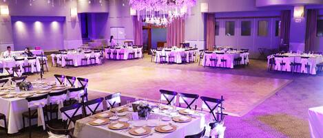 A banquet hall with round tables, white tablecloths, and purple lighting.