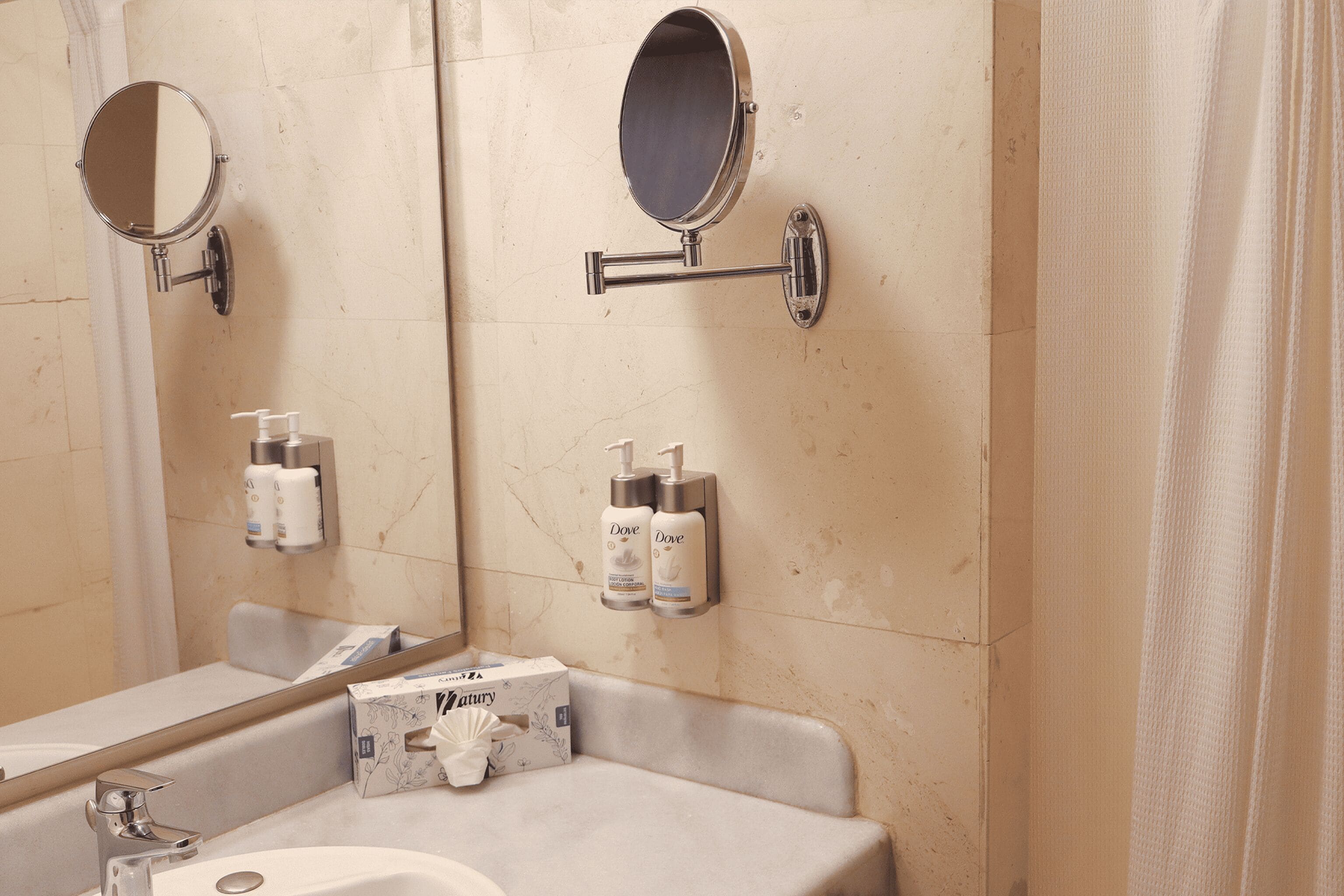 Een badkamer met een wastafel, twee spiegels en toiletartikelen aan de wand.