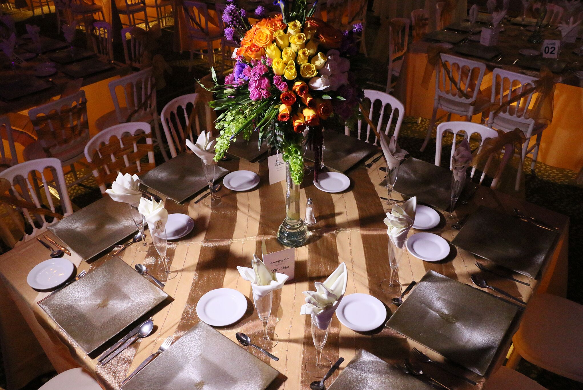 Una mesa de comedor dispuesta con platos blancos, cubiertos y un centro de mesa con flores.