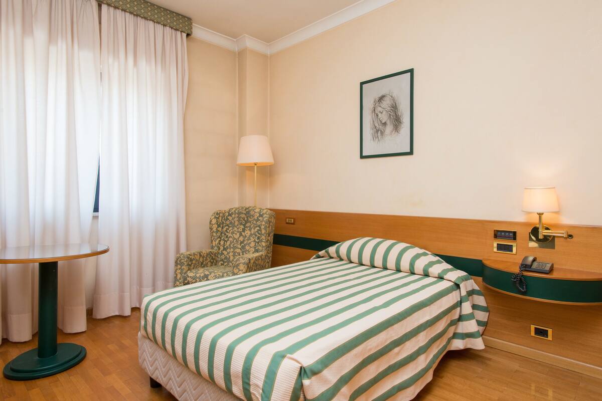 Une chambre d’hôtel avec un lit, une chaise, une table et une lampe.