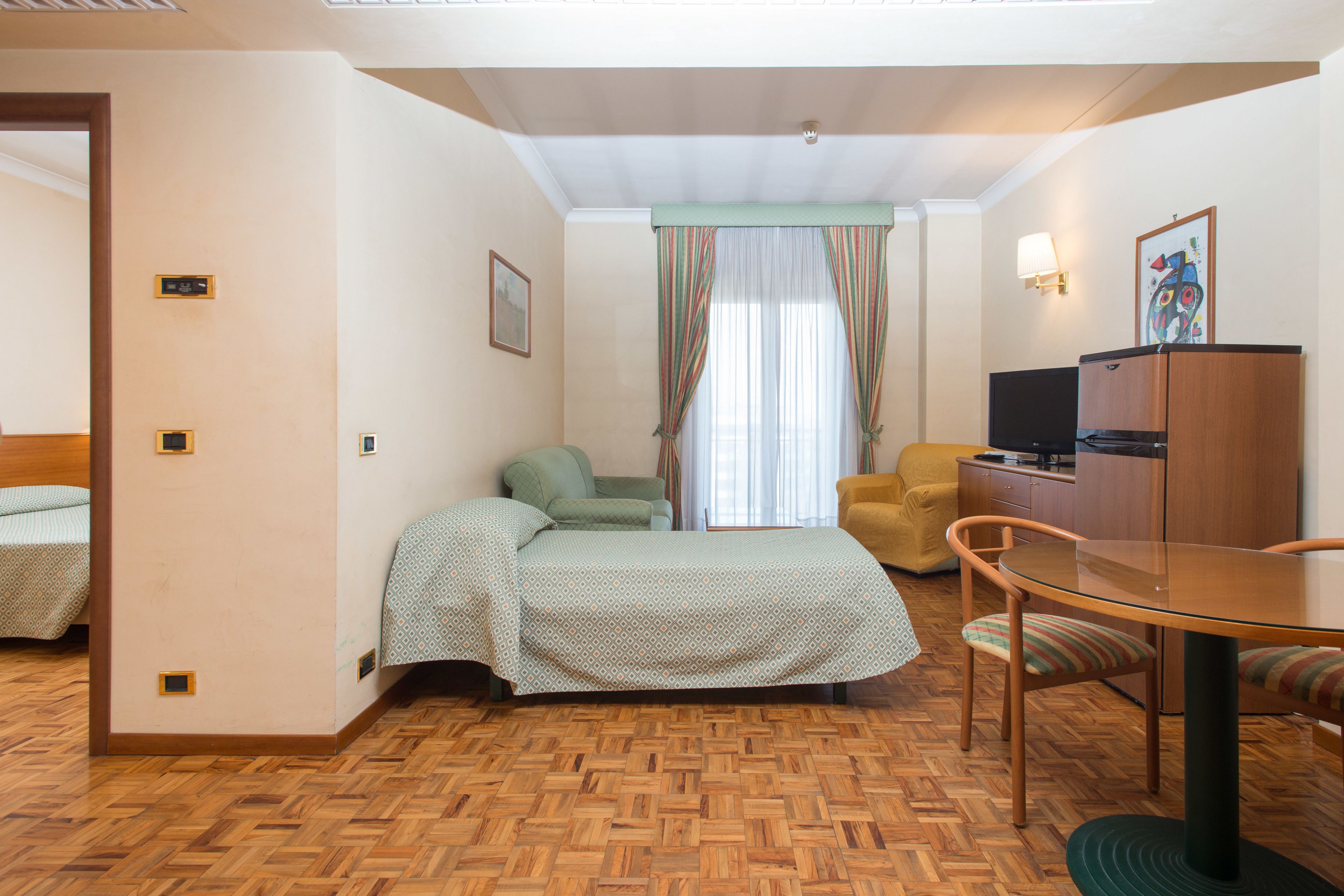 Ein Hotelzimmer mit einem Bett, einem Schreibtisch, einem Stuhl, einem Fernseher und einem Kleiderschrank.