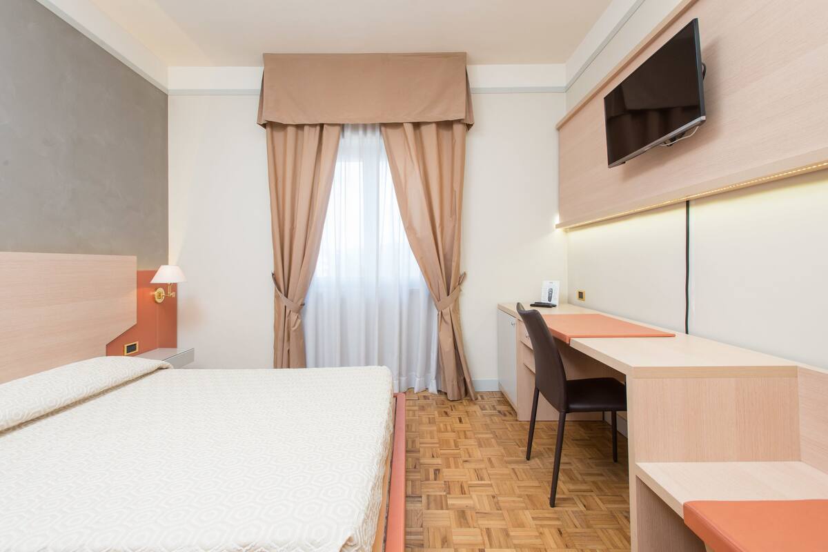 Une chambre d’hôtel équipée d’un lit, d’un bureau, d’une chaise, d’une télévision et de rideaux.