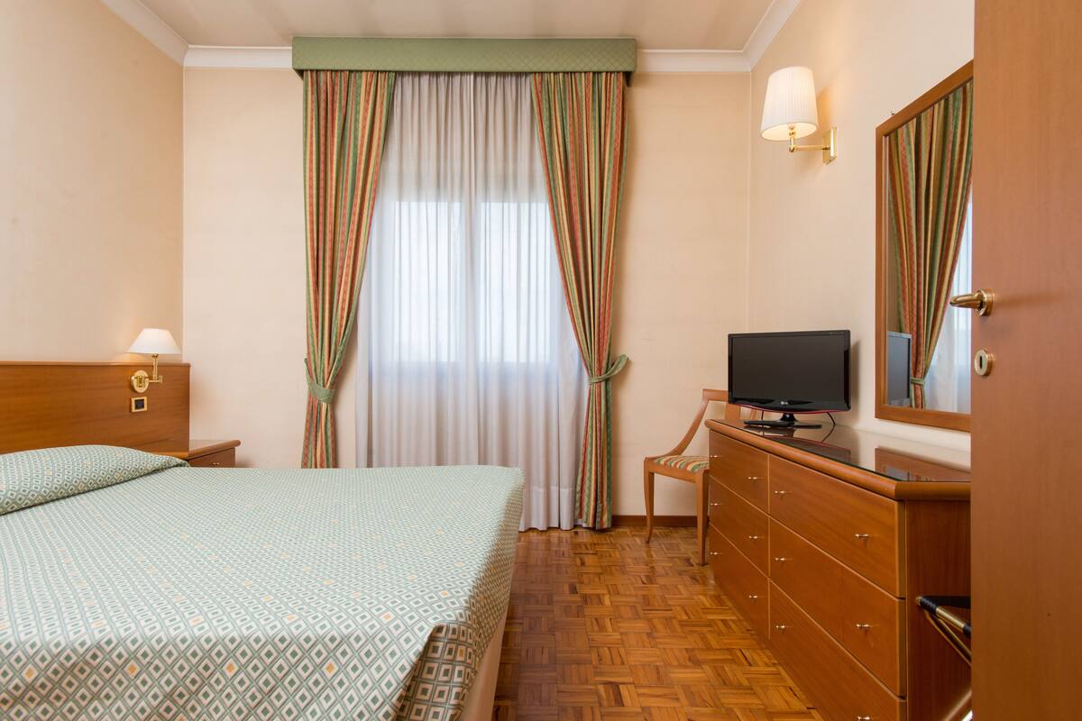 Une chambre d’hôtel avec un lit, une télévision, une commode et un miroir.