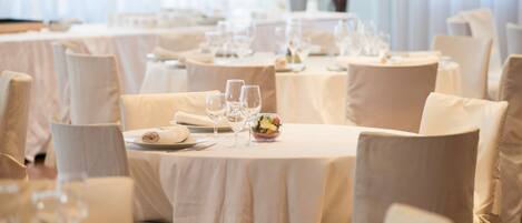 A dining area with round tables, each set with white tablecloths, plates, cutlery, and wine glasses.