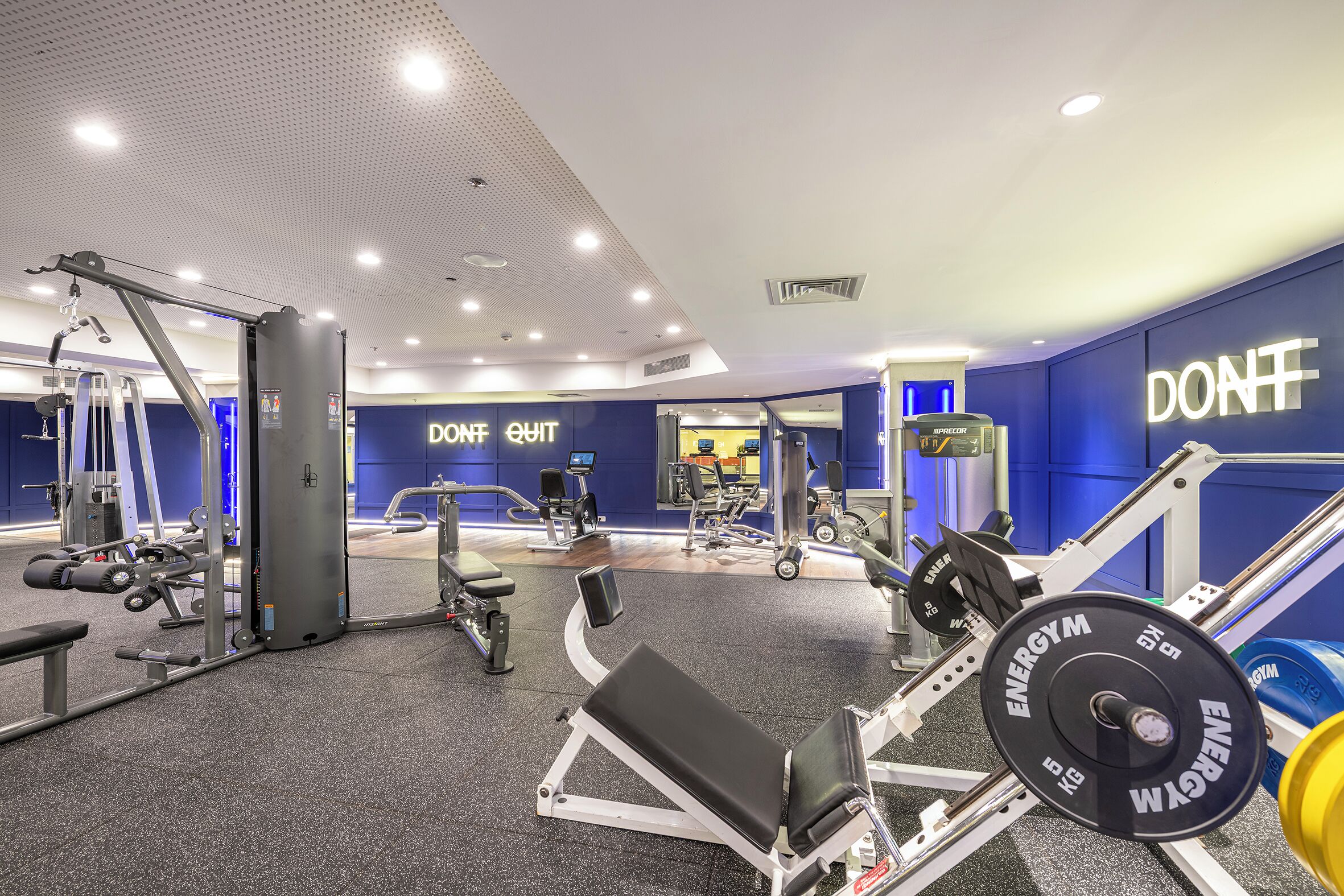 A gym with weightlifting equipment, benches, and a wall with motivational text.