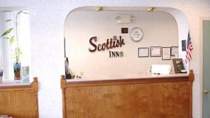 A reception desk with the sign 'Scottish Inns' and a small American flag. There are framed certificates or awards on the wall behind the desk. - Scottish Inns (Commerce)