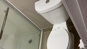 A bathroom with a toilet, a glass shower enclosure, and wooden flooring. - Scottish Inns (Commerce)