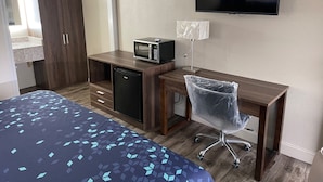 A hotel room with a bed, a desk with a microwave, a TV, and a chair. - Scottish Inns (Commerce)