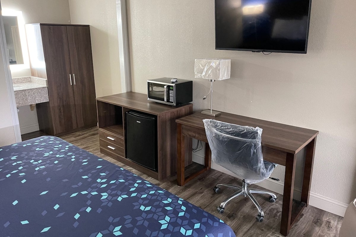 A hotel room with a bed, a desk with a microwave, a TV, and a chair.