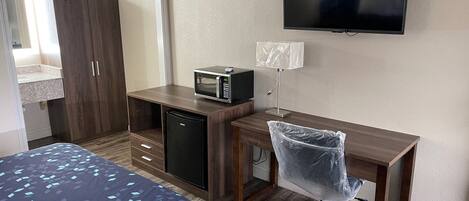 A hotel room with a bed, a desk with a microwave, a TV, and a chair.