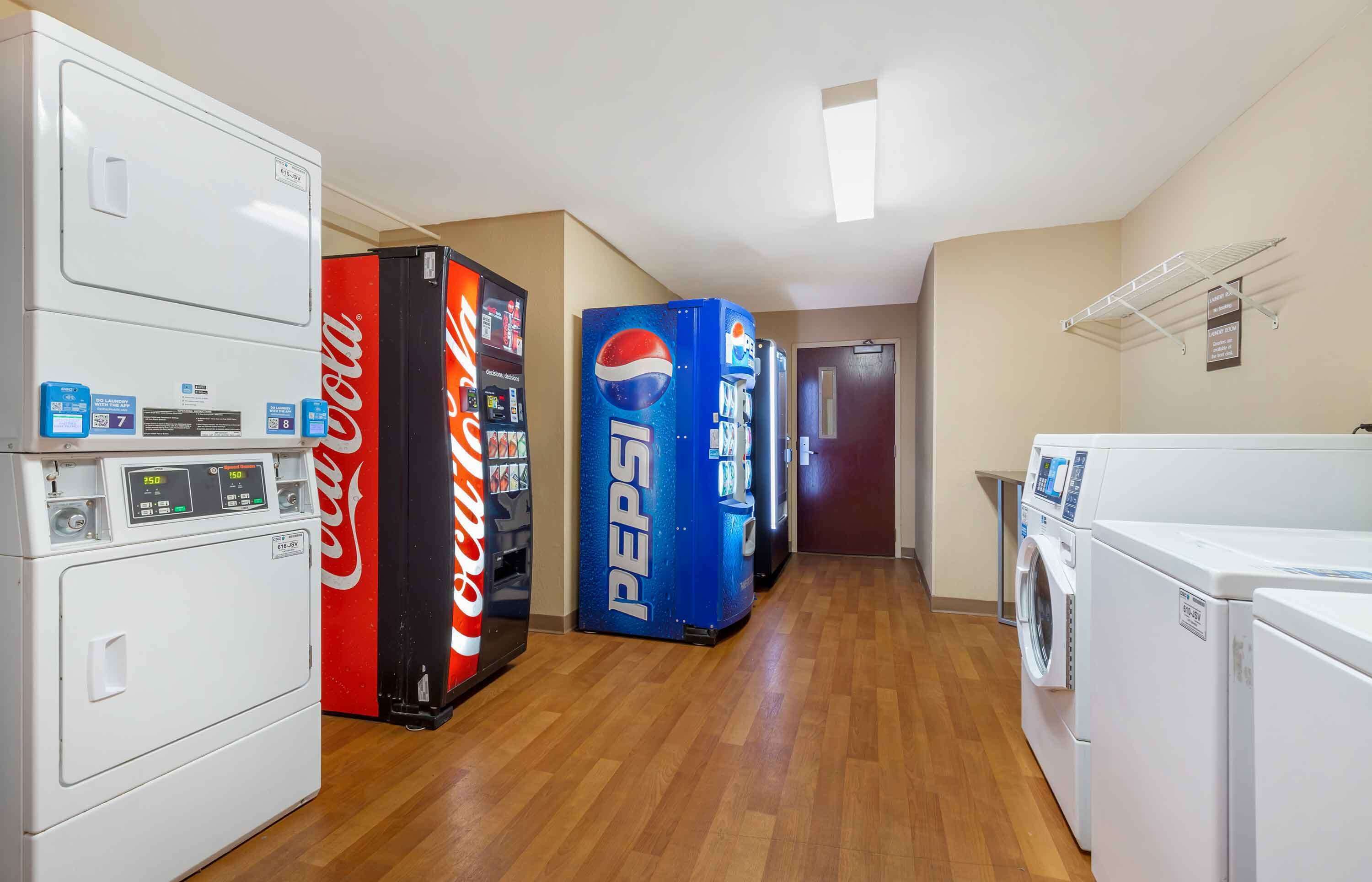 Une buanderie équipée d’un lave-linge, d’un sèche-linge et de distributeurs automatiques, notamment de Coca-Cola et de Pepsi.