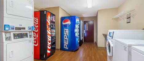 Un cuarto de lavandería con lavadora, secadora y máquinas expendedoras que ofrecen Coca-Cola y Pepsi.