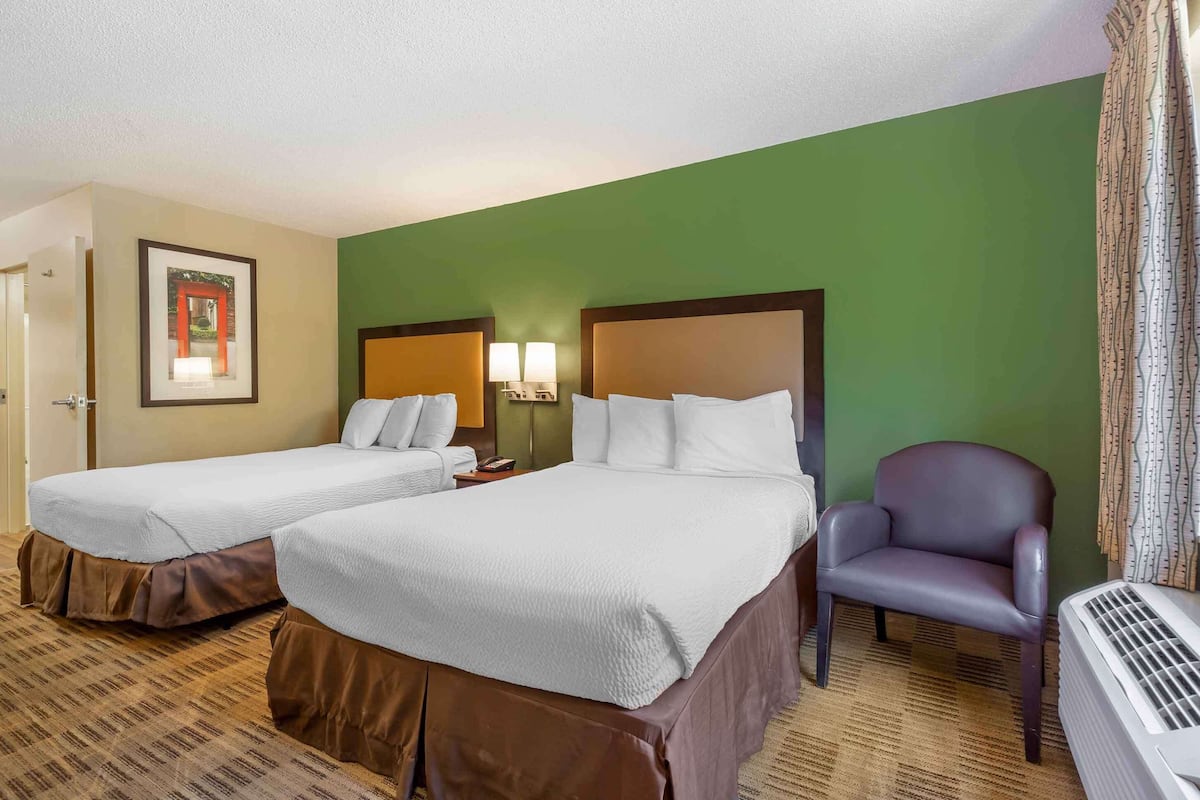 Une chambre d’hôtel avec deux lits, une chaise, un radiateur fixé au mur et un tableau encadré accroché au mur.