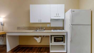 A compact kitchen with white cabinets, a built-in microwave, and a refrigerator.
