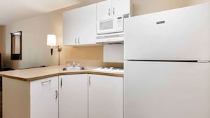 Een moderne keuken met witte kastjes, een magnetron, een koelkast, een spoelbak en een wandlamp.