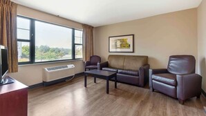 Een woonkamer met een groot raam, een bank, twee fauteuils, een salontafel en een televisie op een dressoir.