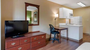 A compact hotel room with a TV on a wooden dresser, a desk with a chair, a kitchenette with a microwave and refrigerator, and a mirror on the wall. - Extended Stay America Suites Atlanta Perimeter Crestline (Atlanta)