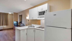 A compact kitchen with white cabinets, a microwave, a refrigerator, a sink, and a small dining area with a chair and a table. - Extended Stay America Suites Atlanta Perimeter Crestline (Atlanta)