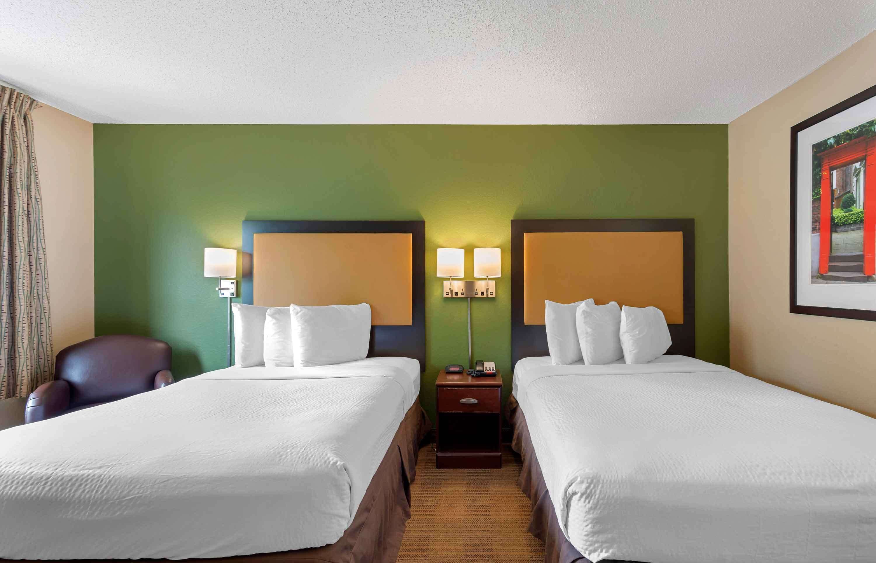 A hotel room with two beds, a nightstand with lamps, a chair, and a framed picture on the wall.