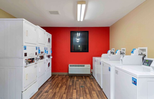 A laundry facility with multiple washing machines and dryers, a red wall, and a wooden floor.