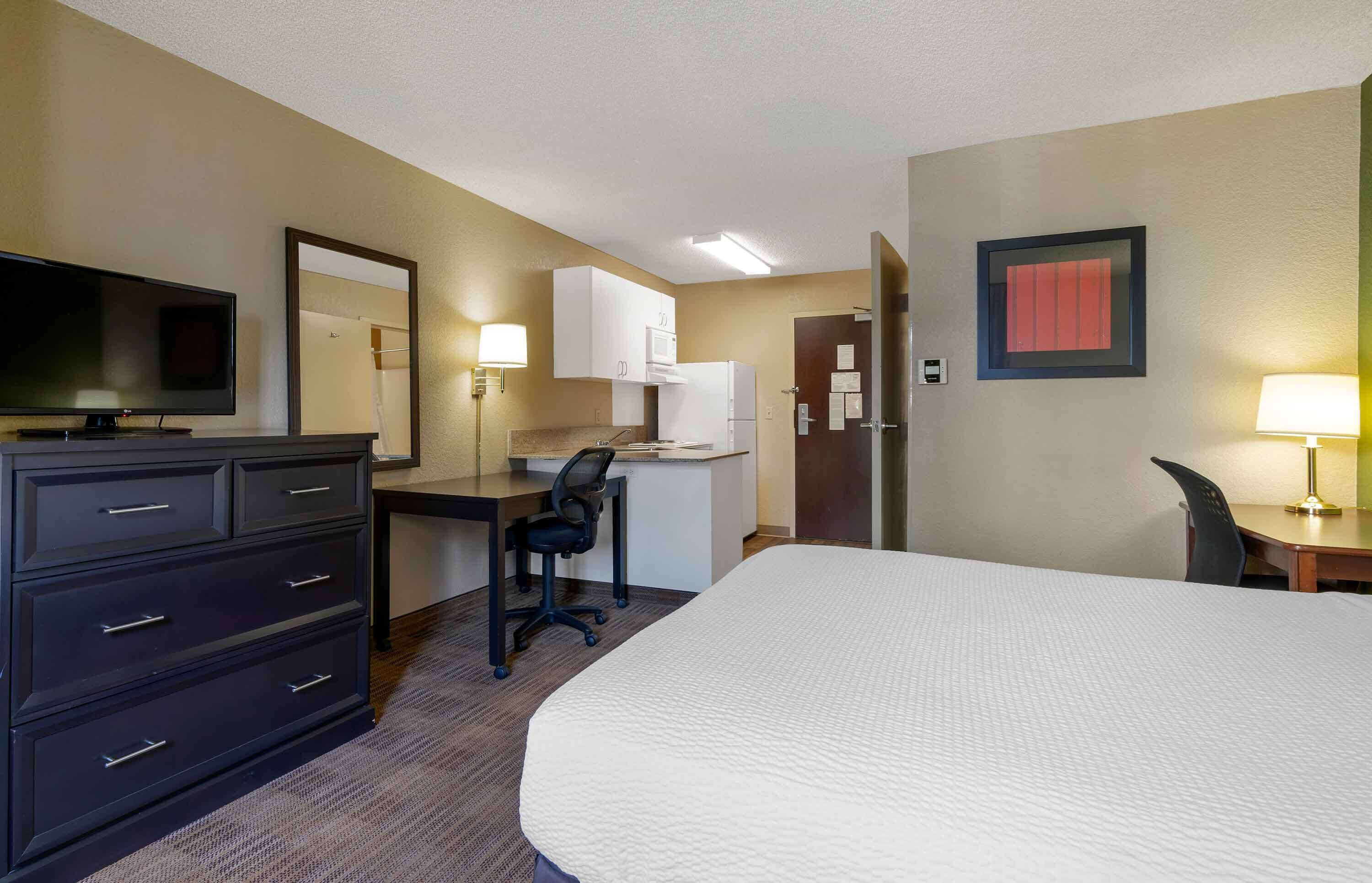 Een hotelkamer met een bed, een bureau met stoel, een televisie, een kast, een magnetron en een koelkast.