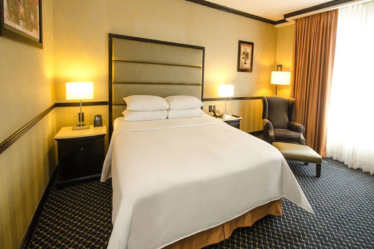 Ein Hotelzimmer mit einem großen Bett, zwei Nachttischen, einem Sessel, einem Schreibtisch und einer Lampe.