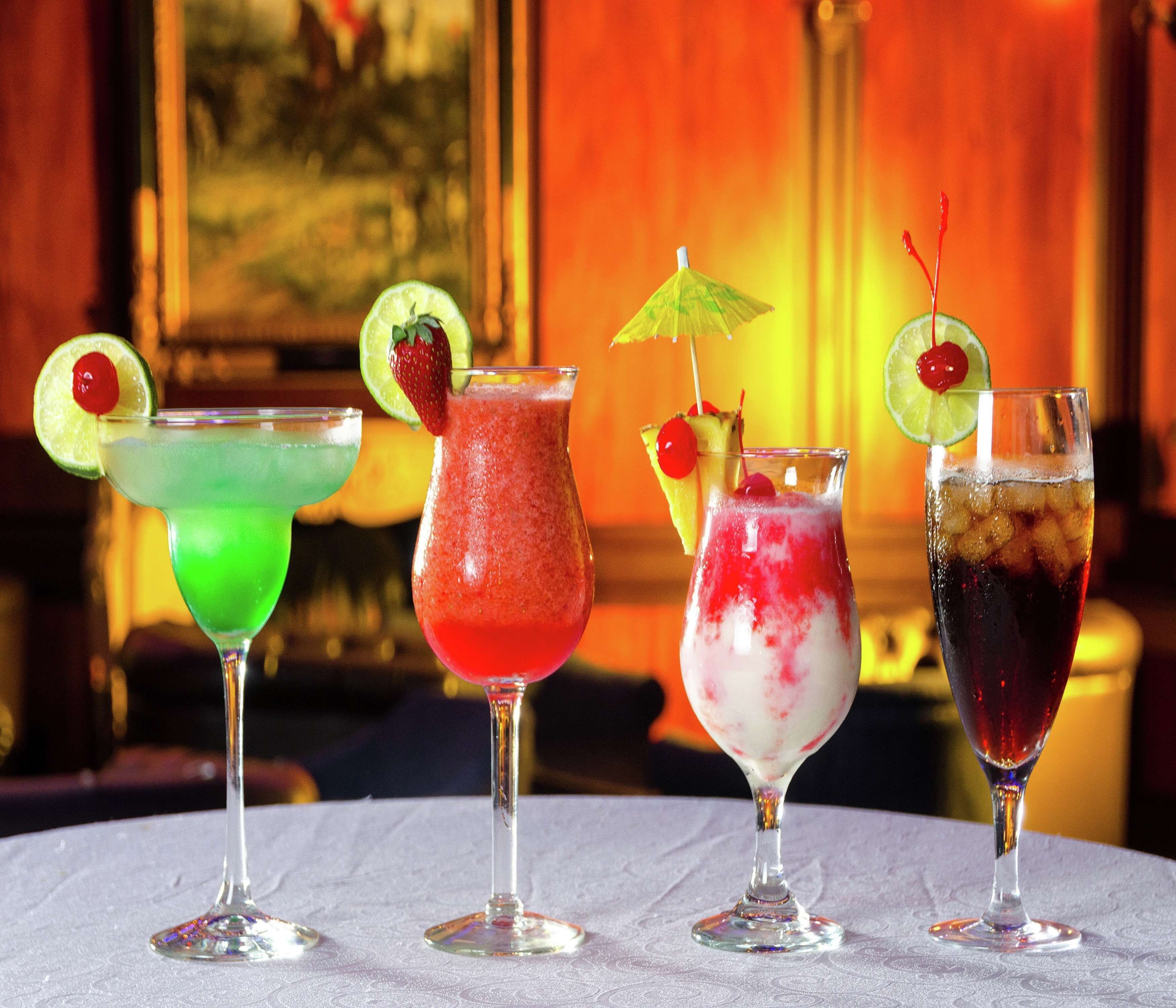 Quatre cocktails sont posés sur une table recouverte d’une nappe à motifs.