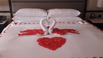 Una cama con un arreglo de pétalos de rosa en forma de corazón y dos cisnes hechos con toallas.