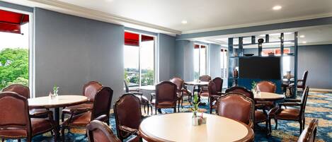 A conference room with round tables and leather chairs, large windows, and a flat-screen TV mounted on the wall.