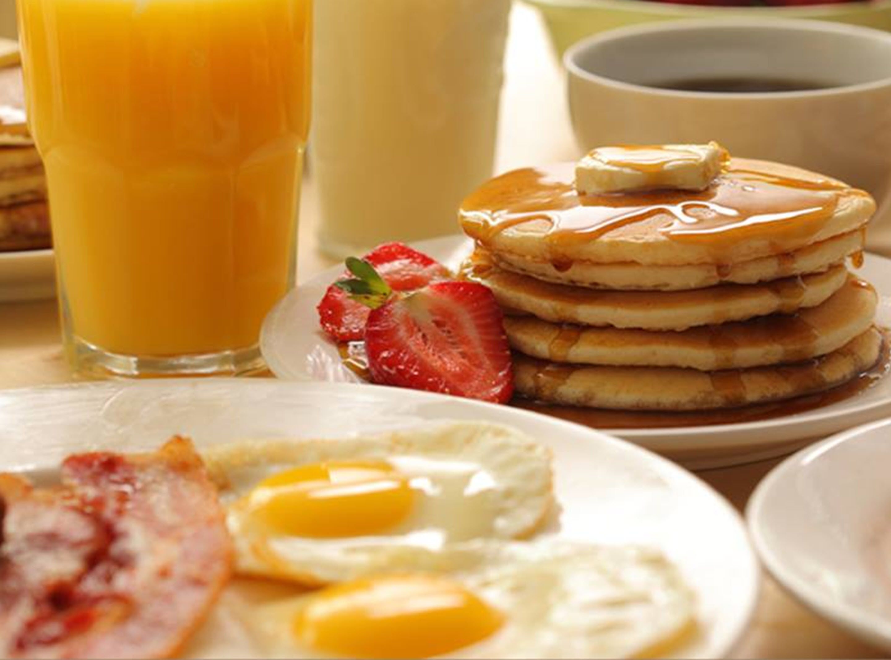 A breakfast setting with pancakes, eggs, bacon, and a glass of orange juice.