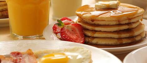 A breakfast setting with pancakes, eggs, bacon, and a glass of orange juice.