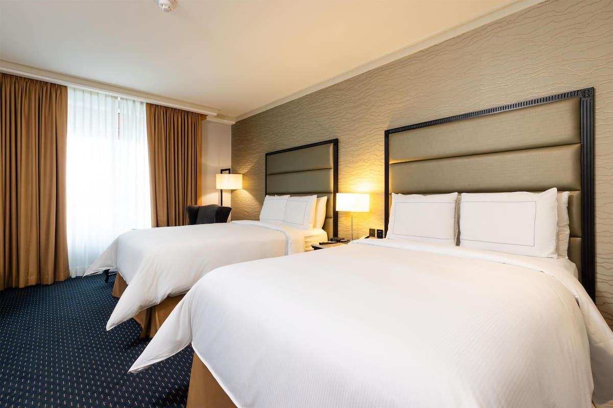 Ein Hotelzimmer mit zwei Betten, einem Schreibtisch, einer Lampe und einem gemusterten Teppich.
