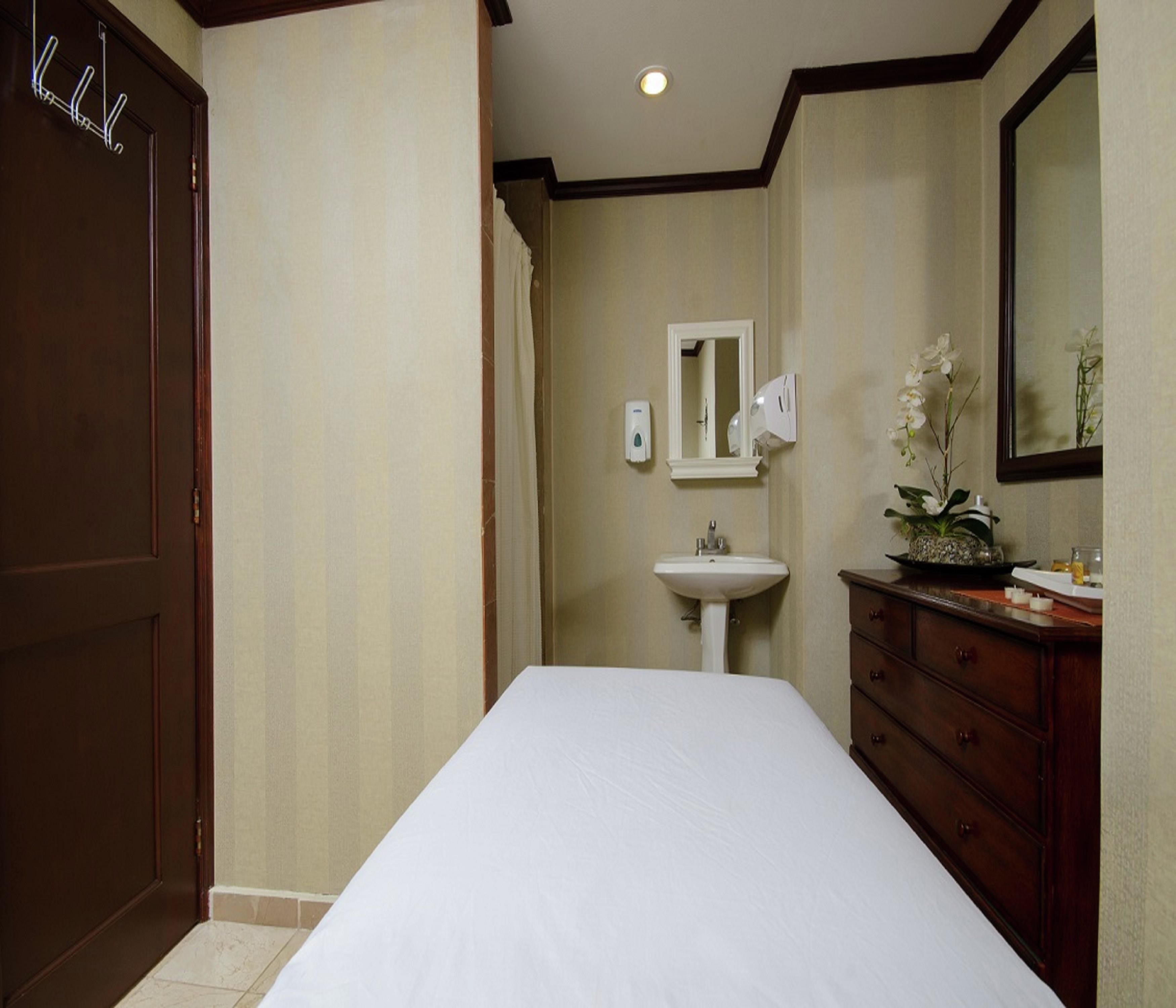 A hotel room with a bed, a dresser, a mirror, a sink, and a door.