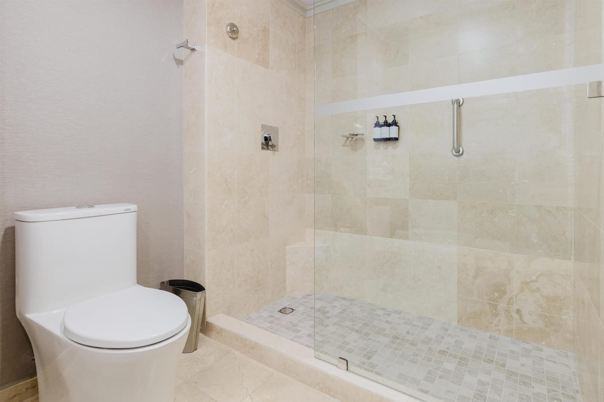 Ein Badezimmer mit Toilette, einer gläsernen Dusche und einem gefliesten Boden.