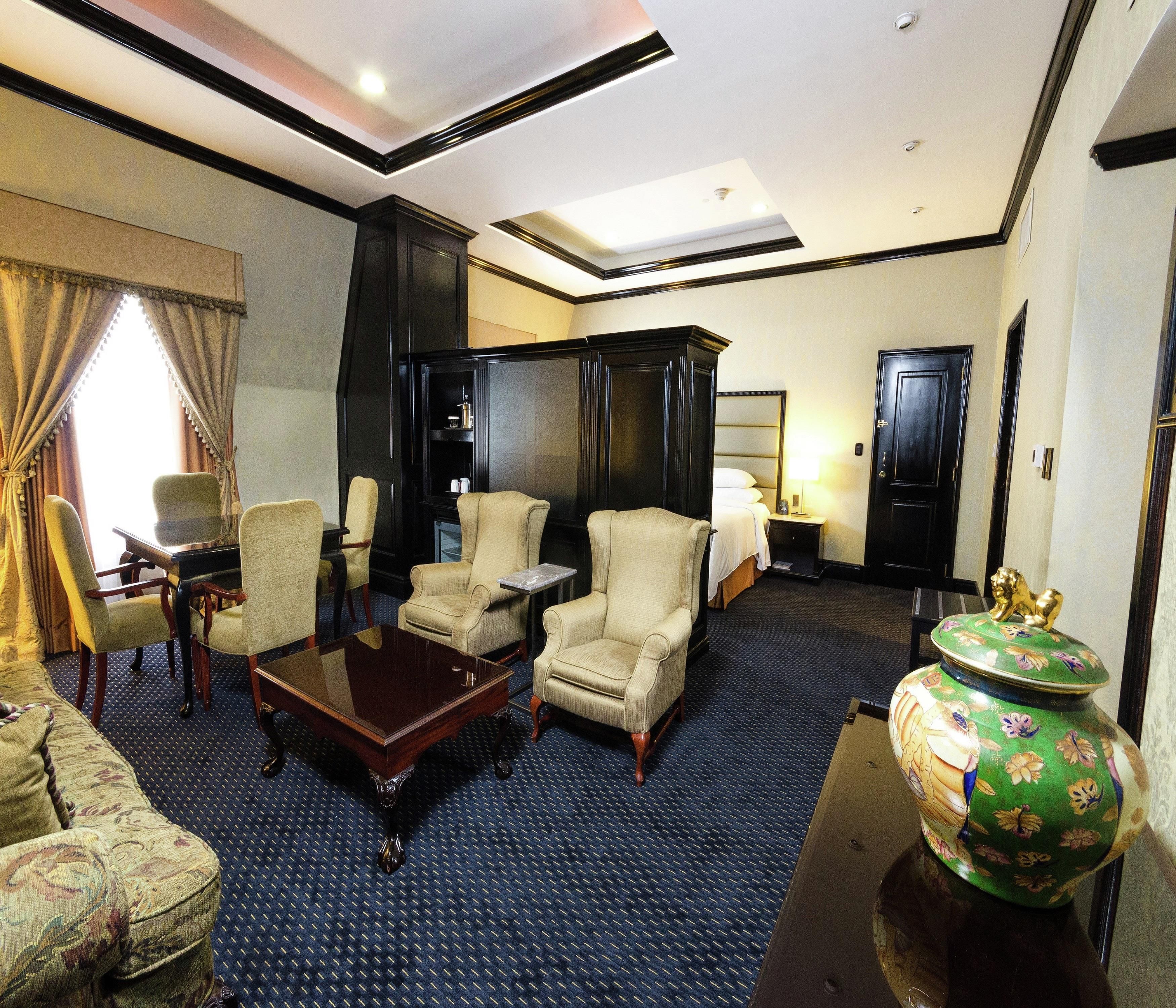 Habitación de hotel con una cama grande, dos sillones, una mesita, un florero decorativo y un armario.