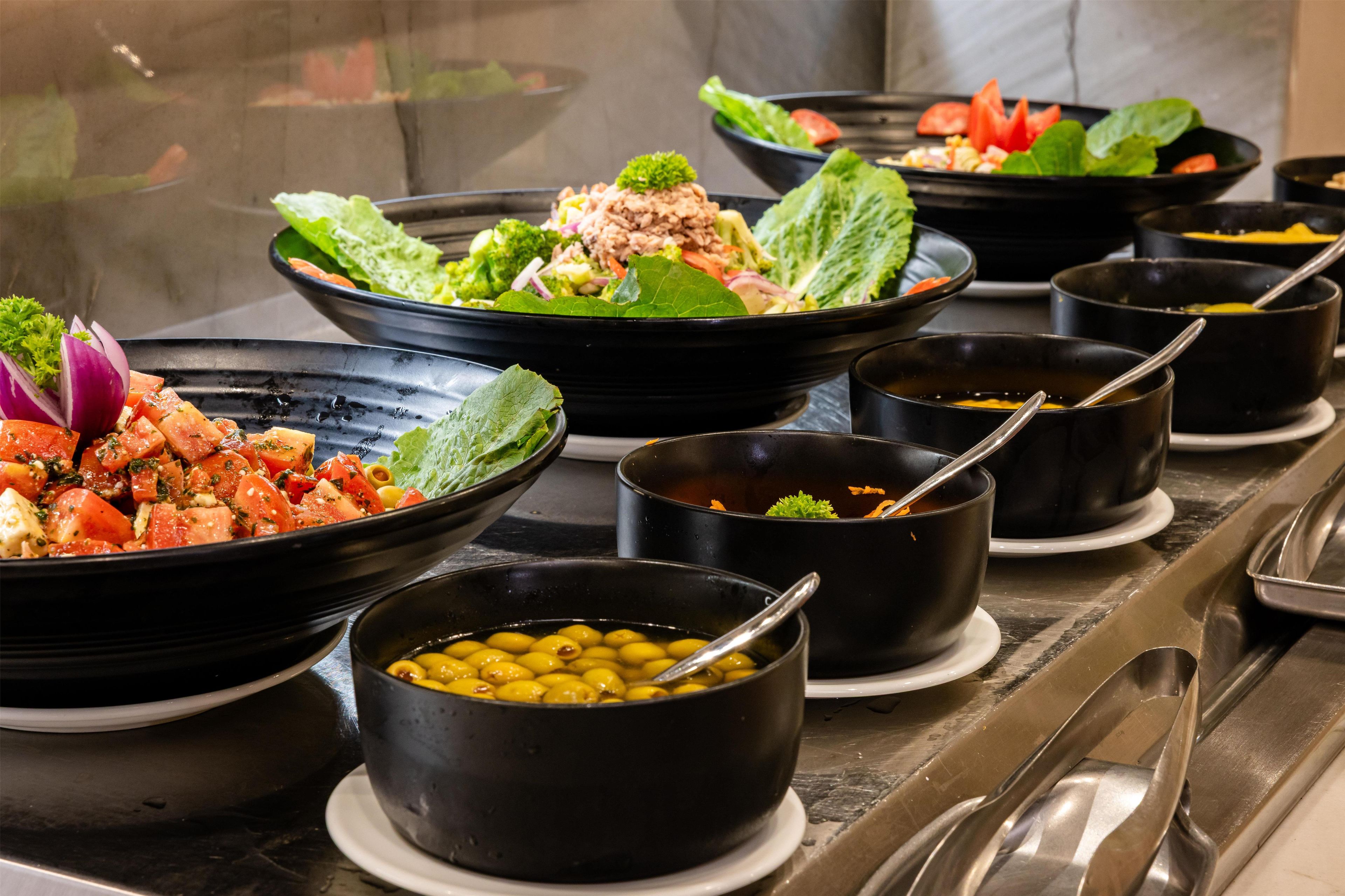 A buffet with various dishes, including salads, vegetables, and bowls of soup.