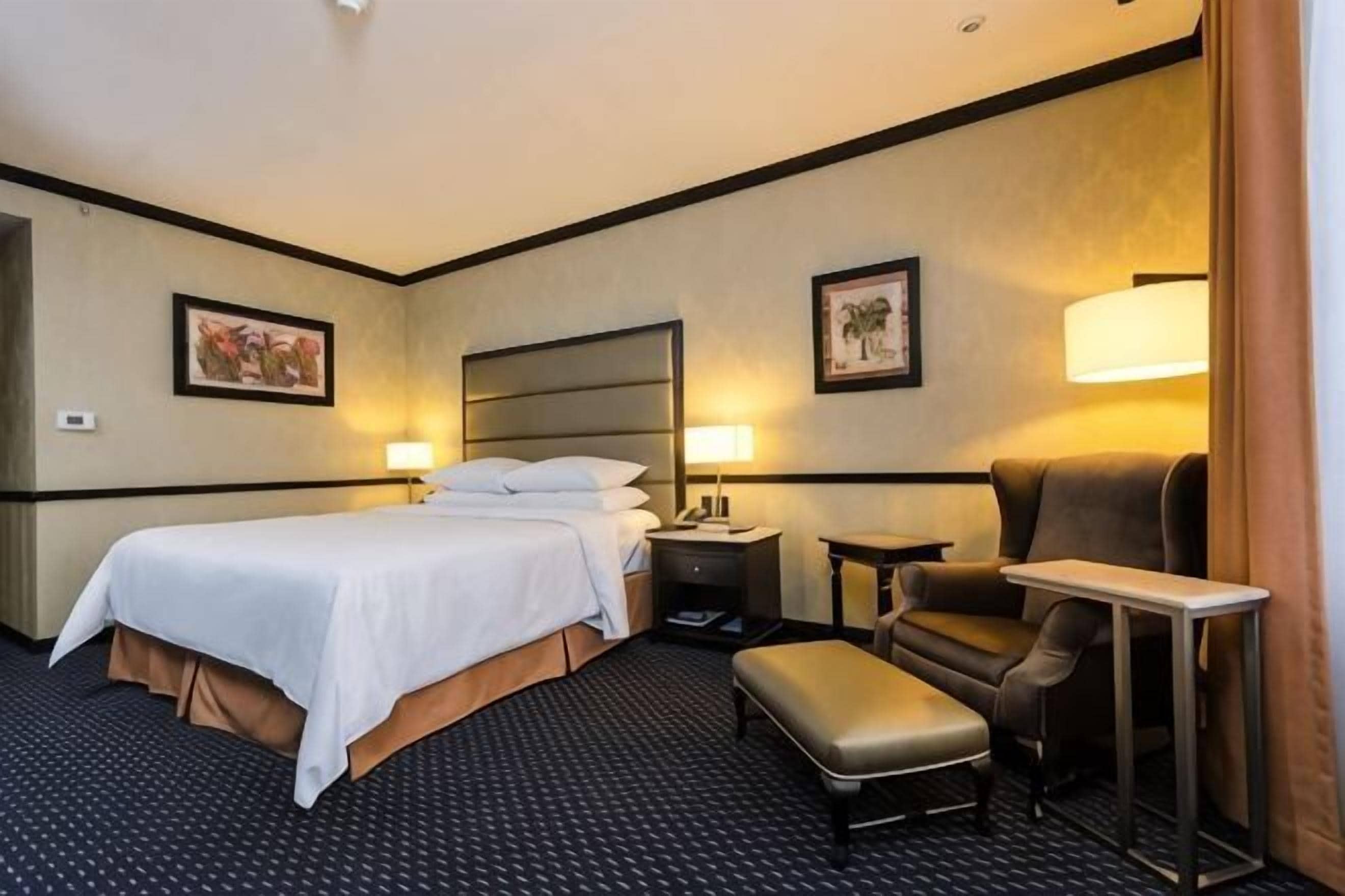 A hotel room with a large bed, two bedside tables, a desk, a chair, and a small table.