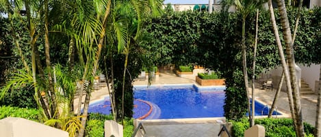Área de piscina com escadas que descem até ela, cercada por palmeiras e vegetação.