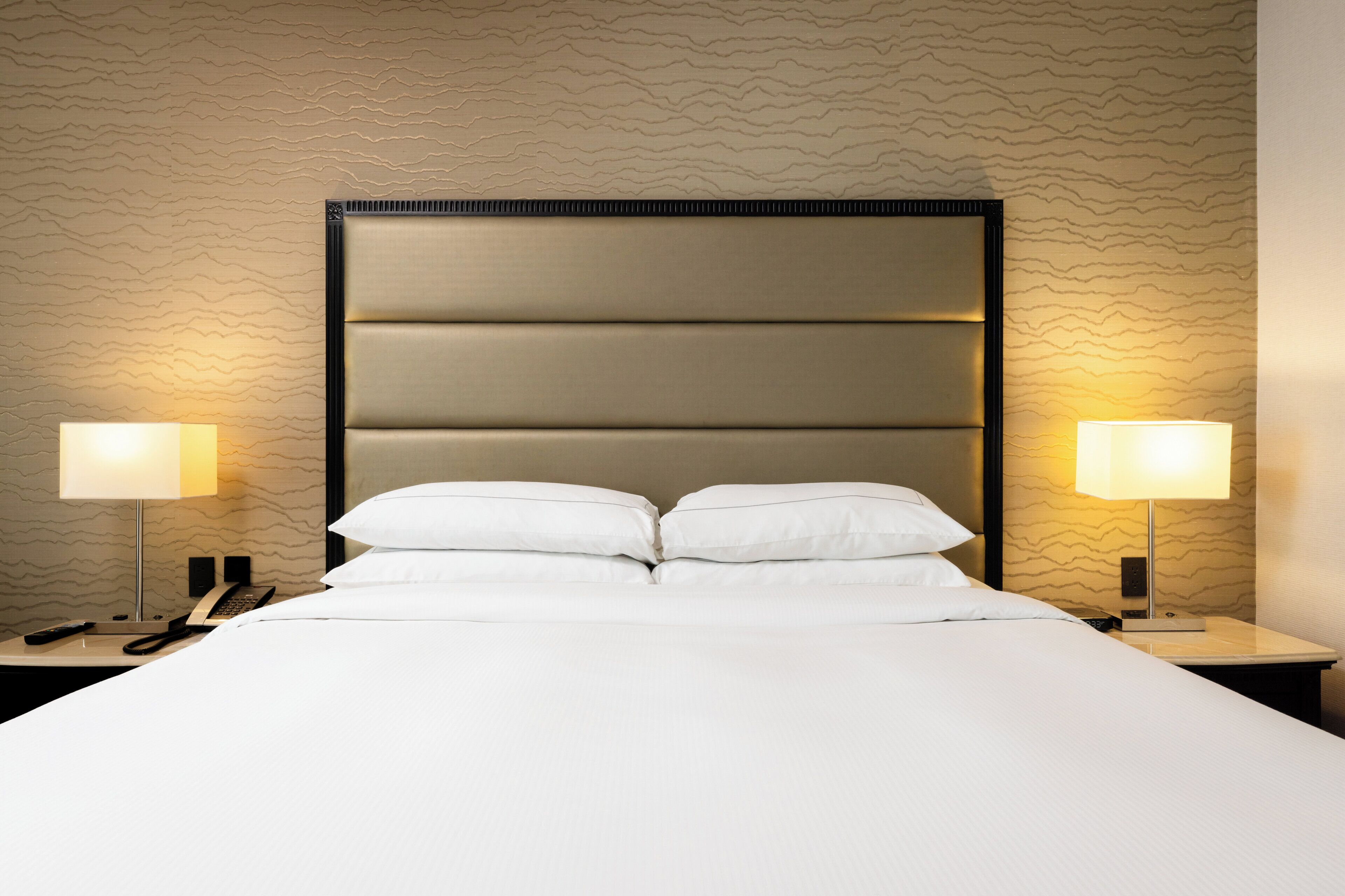 Habitación de hotel con una cama grande, dos lámparas de noche, un teléfono y una pared con textura.