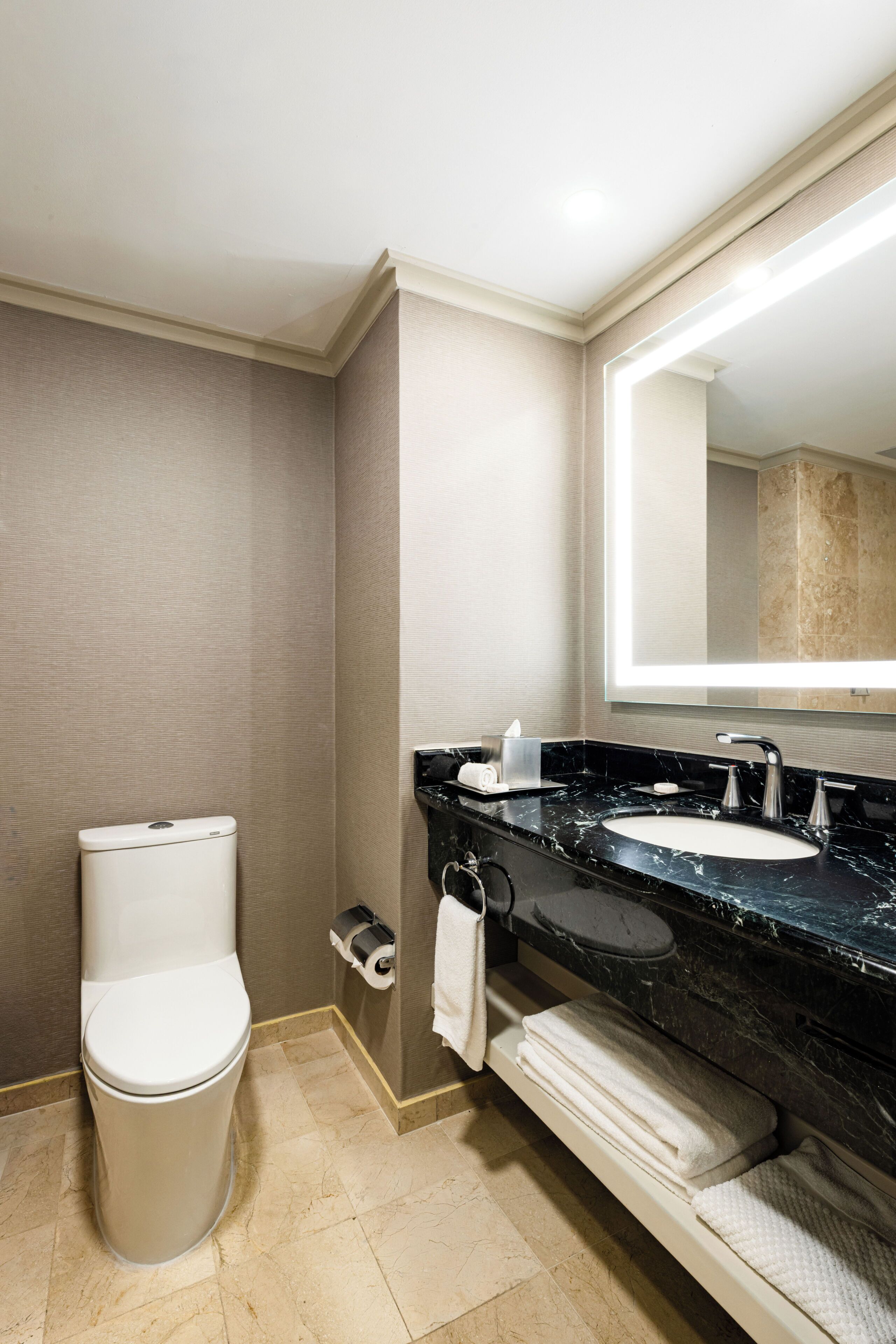 A hotel bathroom with a toilet, a sink with a mirror, and a towel rack.