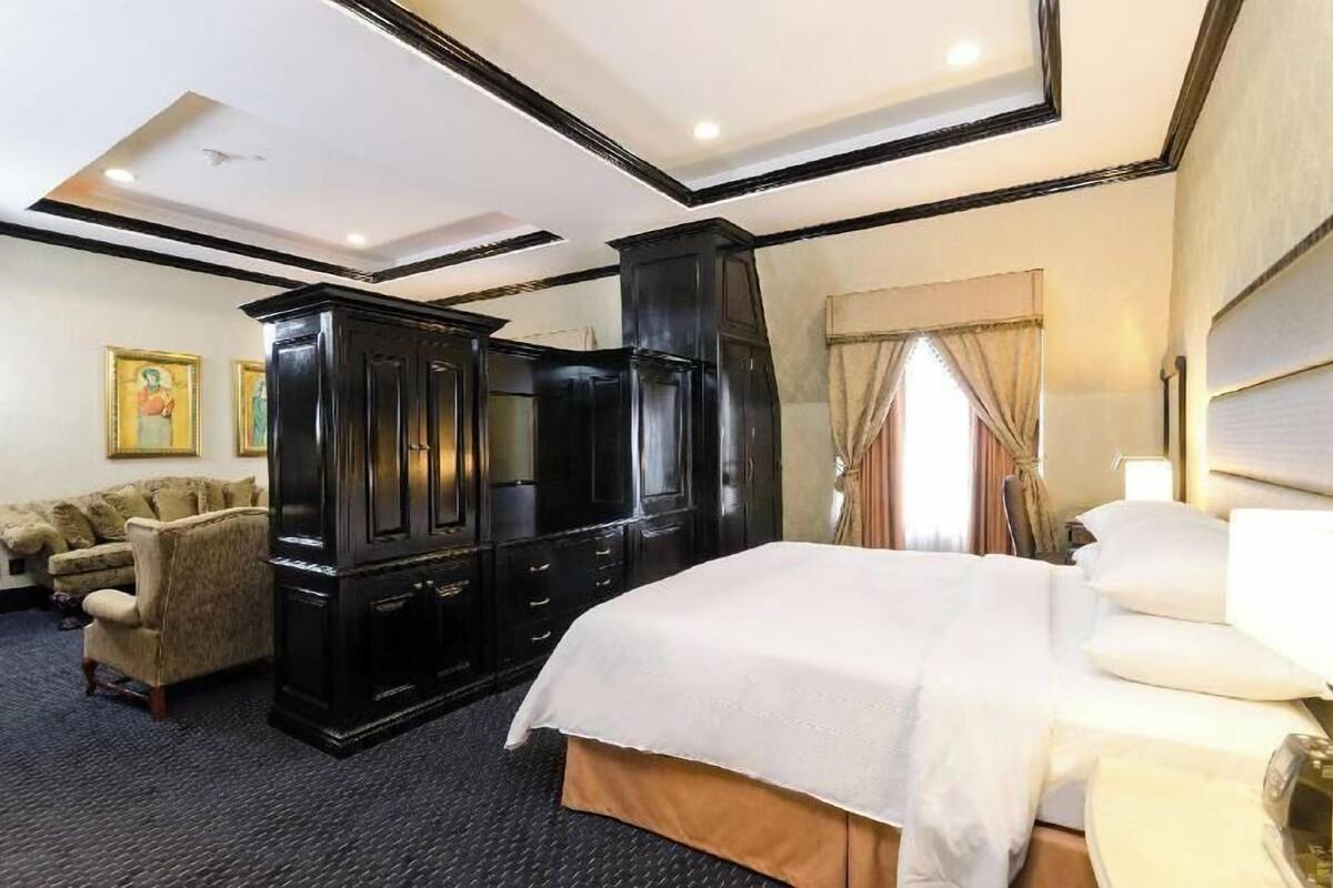 Ein Hotelzimmer mit einem großen Bett, einem dunklen Holzschrank, einer Couch und einem Fernseher.