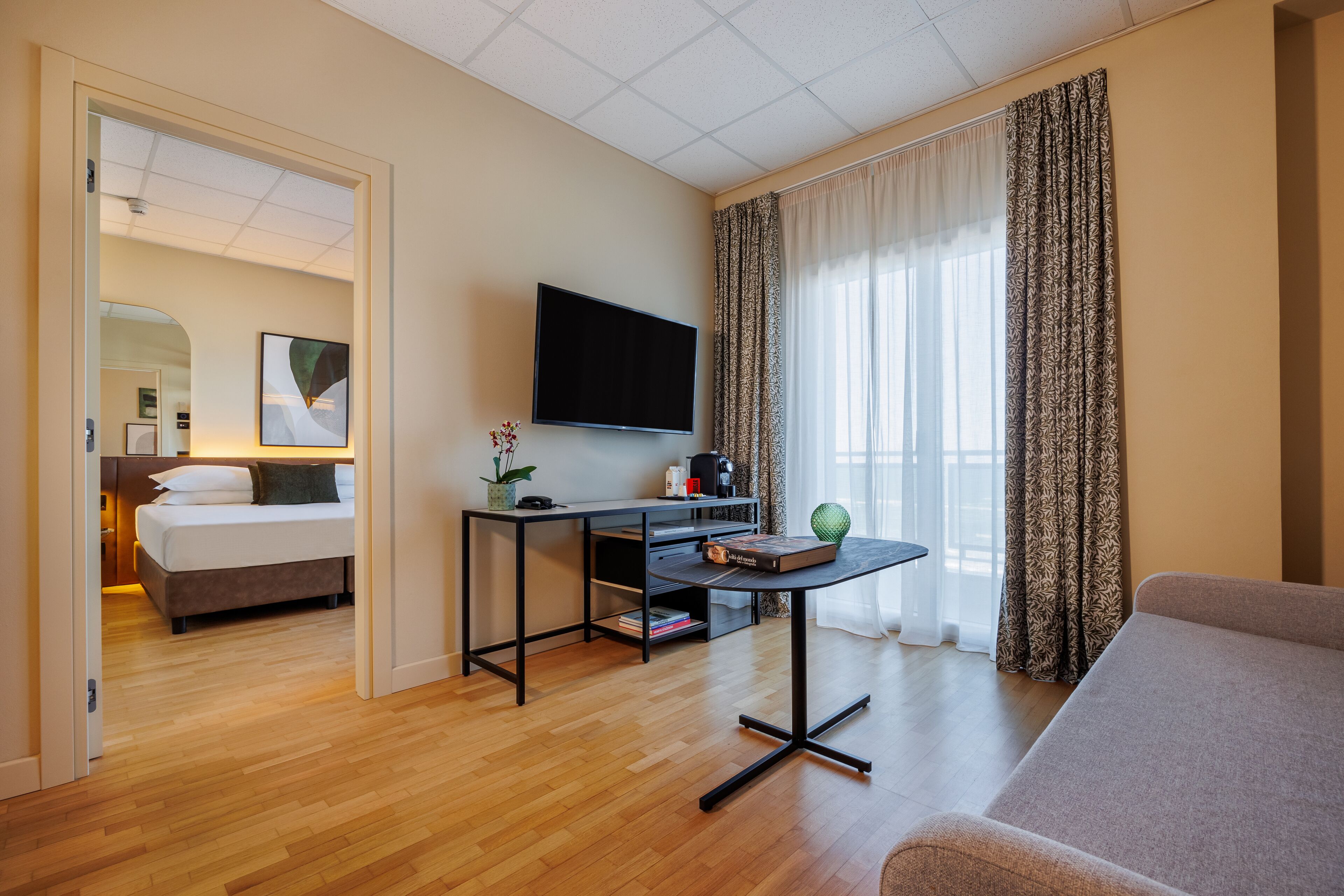 Quarto de hotel com cama, escrivaninha, televisão e sofá.