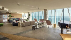 Amplia sala de estar con un piano, sofás y un ventanal con vistas al mar.