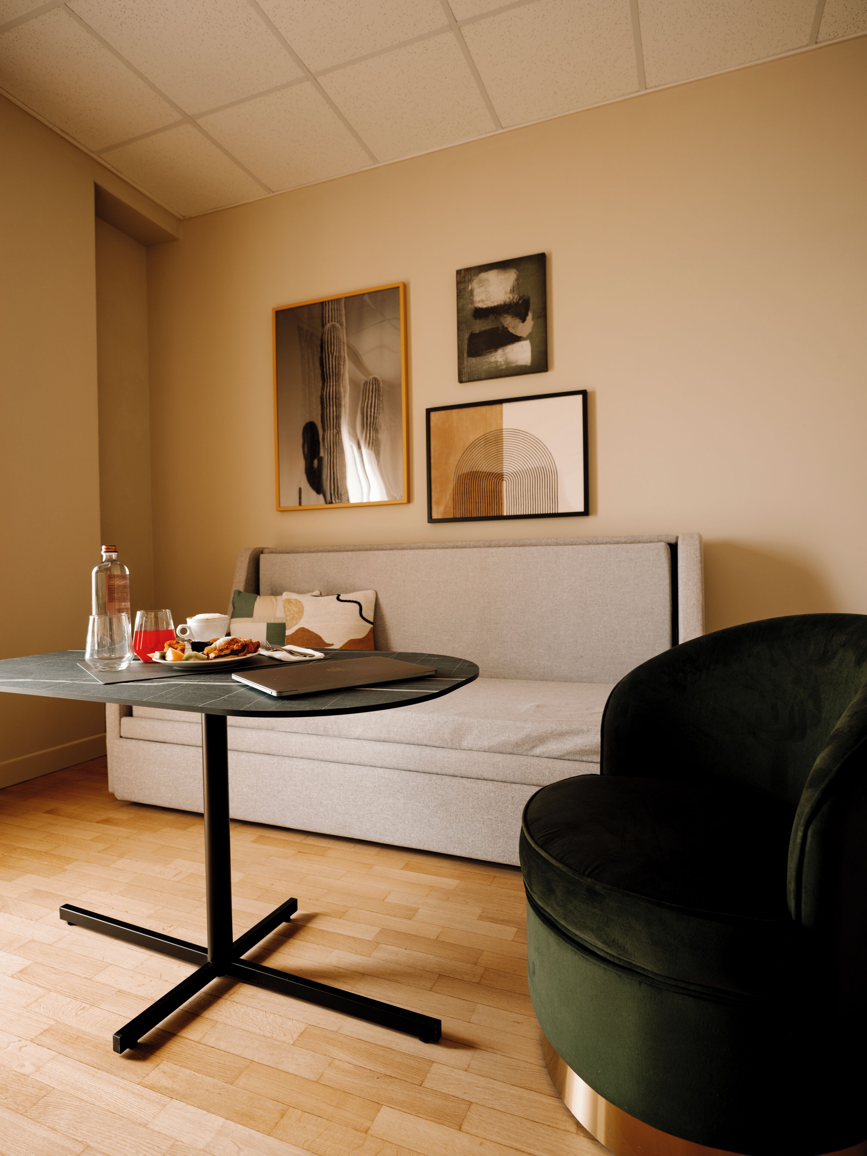 A modern living room with a grey sofa, a black armchair, a round table with a black base, and two framed artworks on the wall.
