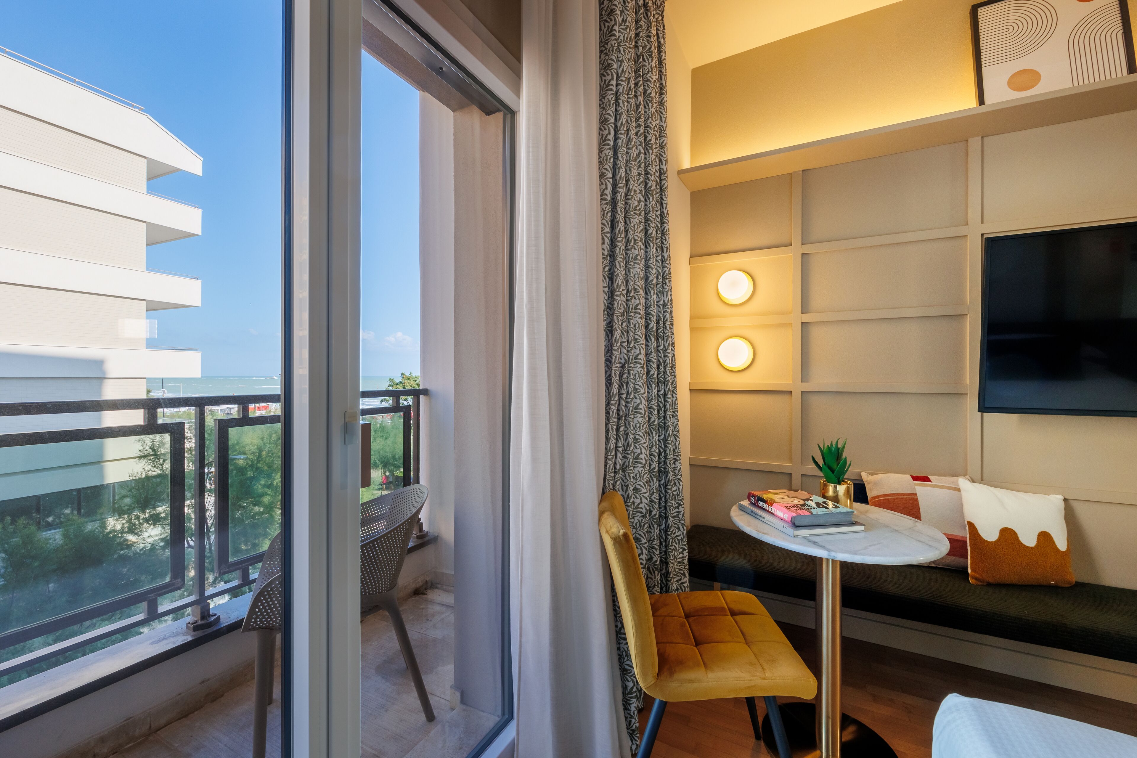 A modern hotel room with a balcony, a sofa, a small table, and a TV.